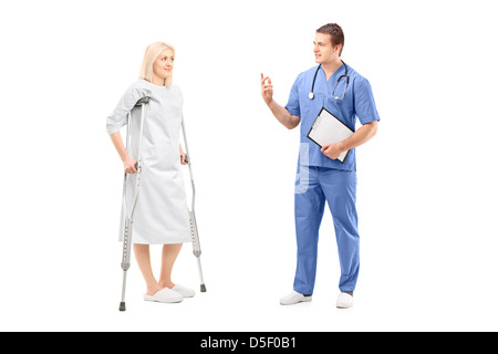 Full length portrait of a blond female patient in hospital gown with crutches and medical practitioner during a conversation Stock Photo