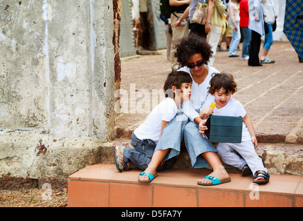 Mother and 2 children using an ipad tablet sitting at the doorstep of St. Paul's Church in Malacca, Malaysia. Stock Photo