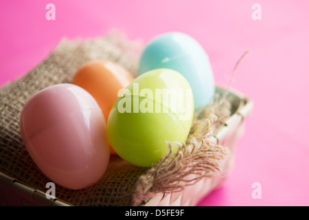 A basket of coloured plastic easter eggs, against a bright pink background Stock Photo