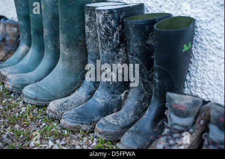 A row of green and black muddy wellington boots all lined up against a wall after a family walk in the English countryside on a farm