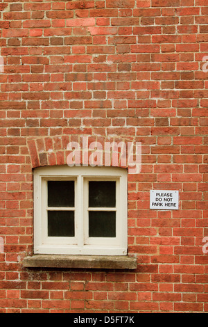 'Please do not park here sign'  screwed to a red brick wall next to a window in Horsham Sussex England Stock Photo