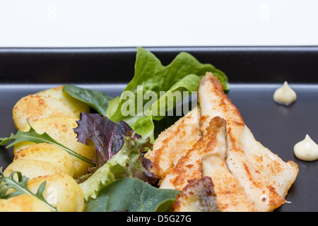 Fried perch fillets with potatoes, lemon and salad in a black plate Stock Photo