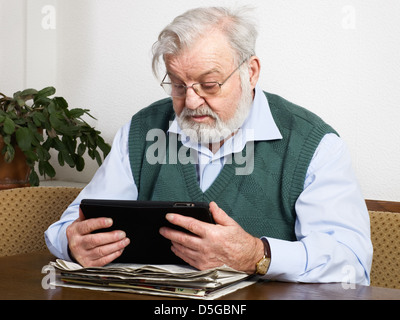 Senior man reading newspaper on digital tablet Stock Photo