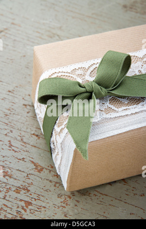 Simple decorative gift box wrapped in brown eco paper, white lace and green bow on wooden vintage background Stock Photo