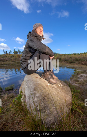 Young woman sitting on rocks near a pond. Stock Photo