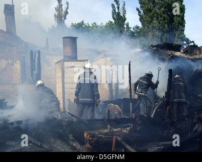 Smoldering remains of a ghetto house with a fireman spraying water firefighters extinguish a fire in an apartment house Stock Photo