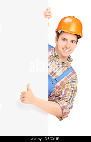 Construction worker posing and giving thumb up on a panel isolated against white background Stock Photo