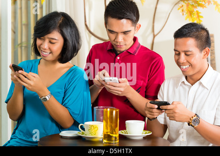 Asian people having fun together with mobile phone and drinking coffee or cocktail Stock Photo