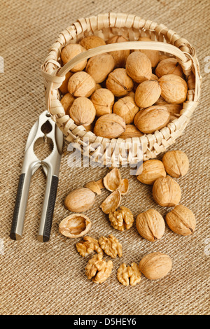 Walnuts in wicker basket and nutcracker on linen background Stock Photo