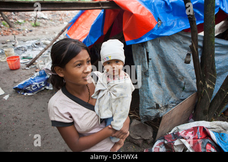 A young Nepalese mother holds her baby outside their plastic tent home in United Nations Park, a slum in Paurakhi Basti, Nepal. Stock Photo