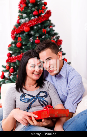 Portrait of a happy young couple sitting in front of a beautiful Christmas tree Stock Photo