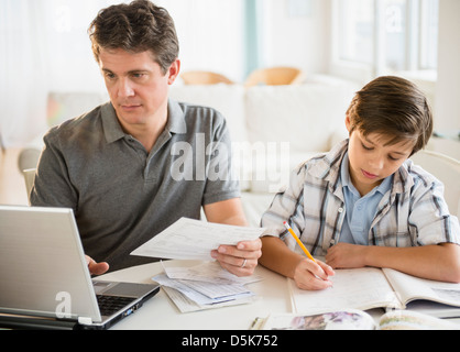 Father working on laptop and son (8-9) doing homework Stock Photo