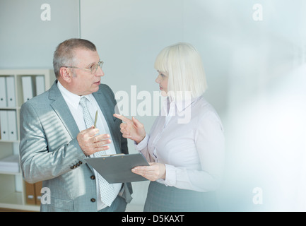 Confident mature businessman and his colleague looking at one another while discussing document at meeting Stock Photo