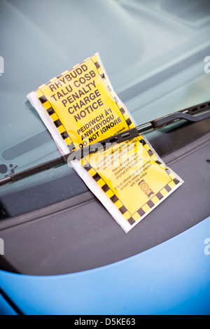 A bilingual penalty charge notice parking ticket in both English and Welsh beneath a car windscreen wiper. Stock Photo