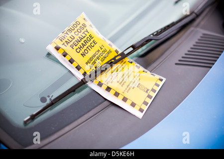 A bilingual penalty charge notice parking ticket in both English and Welsh beneath a car windscreen wiper. Stock Photo