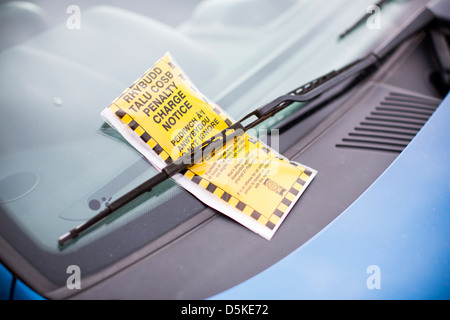 A bilingual penalty charge notice parking ticket in both English and Welsh beneath a car windscreen wiper. Stock Photo