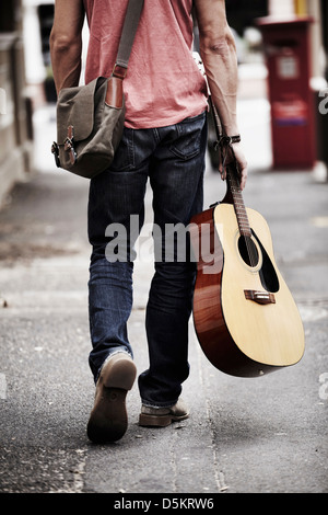 Man with guitar walking down street Stock Photo