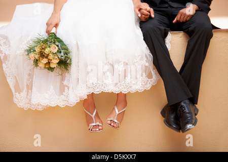 Bride and groom sitting on wall Stock Photo