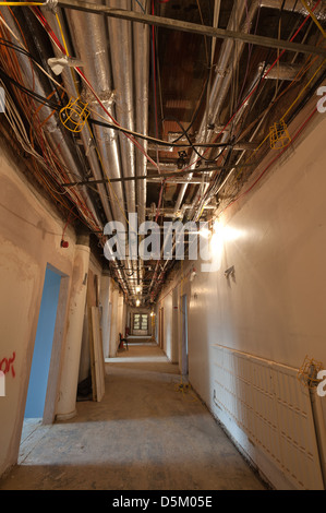 Gloomy empty corridor with exposed pipework and badly organised electrical cabled for networking mains electricity Stock Photo