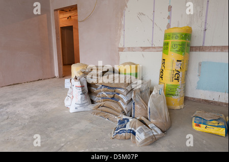 Bags of cement plaster rockwool insulation piled up inside a newly plastered room with concrete floor and entrance to hallway Stock Photo