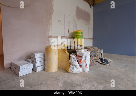 Bags of cement plaster rockwool insulation piled up inside a newly plastered room with concrete floor and entrance to hallway Stock Photo
