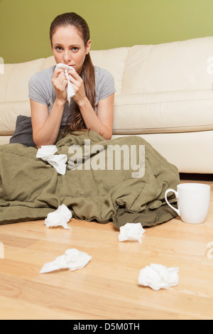 Woman in living room blowing her nose Stock Photo