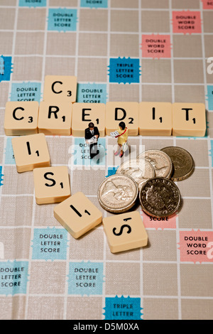 Tiles on Scrabble board words spelling credit crisis, with toy man and woman figures and English money pound coins business finance recession concept Stock Photo