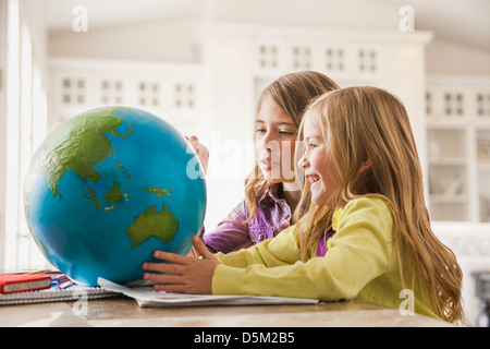 Two girls (6-7) doing homework with globe Stock Photo