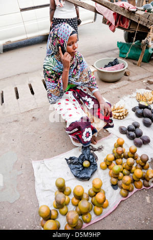 Young Muslim Woman selling vegetables and using cell phone on street in Moshi;Africa;East Africa;Tanzania; Stock Photo