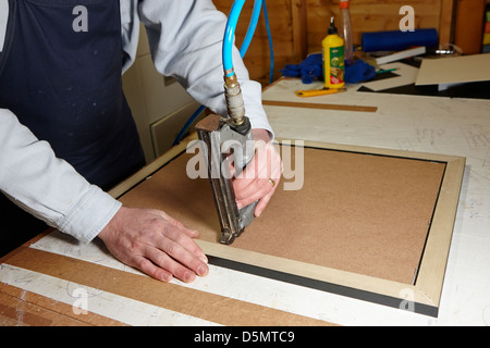 framer using air nailer to nail backboard on a picture frame in a framing workshop Stock Photo