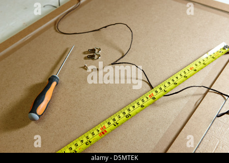 measuring tape screwdriver hanging strings and fixings on the back of a picture frame in a framing workshop Stock Photo