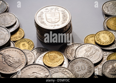 A pile of current, legal tender Swiss Francs (CHF), with a stack of 5 Franc coins spot lit in the center. Stock Photo