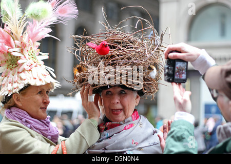 One woman adjusts another's hat, which resembles a bird's nest, as a man  takes a picture, at New York's City's Easter Parade Stock Photo
