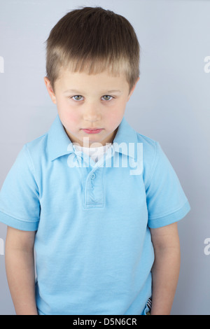 Sad and forlorn 5 year old boy with a light blue shirt looking at camera with head slightly down. Stock Photo