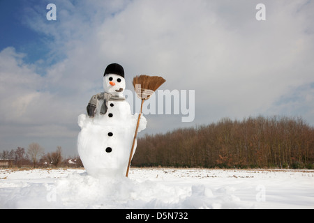 Decorated happy snowman with carrot nose, hat, pipe, scarf and broom in the snow in winter Stock Photo