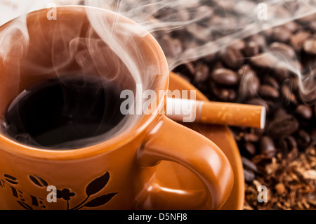 A cigarette with an ashtray and a cup of cappuccino,black coffee with a  cigarette,a tobacco product in an ashtray on a wooden table in a cafe Stock  Photo