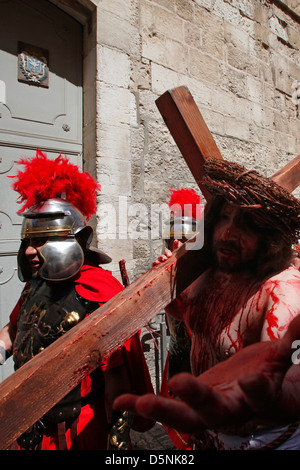 A Christian devotee dressed as Jesus Christ carries a wooden cross reenacting the Stations of the Cross during Good Friday procession along Via Dolorosa street believed to be the path that Jesus walked on the way to his crucifixion in the Old City East Jerusalem, Israel Stock Photo