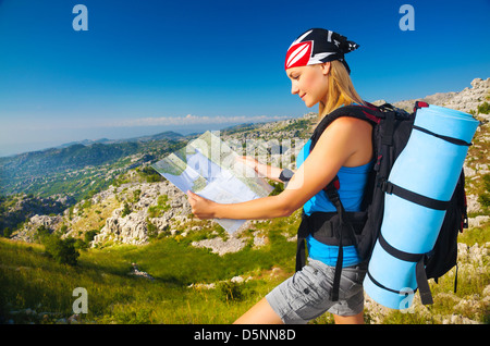 Young sporty woman standing on the peak on mountain watching on map, extreme adventure, happiness and freedom concept Stock Photo