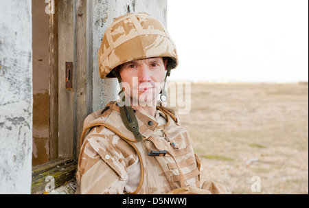 British soldier wearing desert camouflage, looking at the camera and leaning against a derelict building. Stock Photo