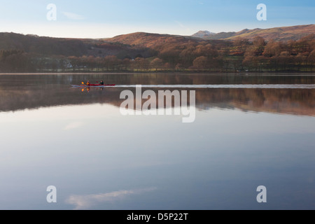 Two men in a Canadian kayak paddle across a very still Coniston water on a beautiful calm winter morning Stock Photo