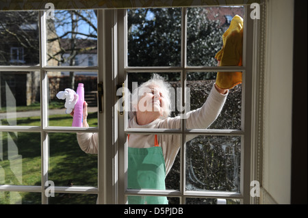 Elderly pensioner cleaning windows of her home in the sunshine Stock Photo