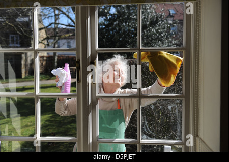 Elderly pensioner cleaning windows of her home in the sunshine Stock Photo