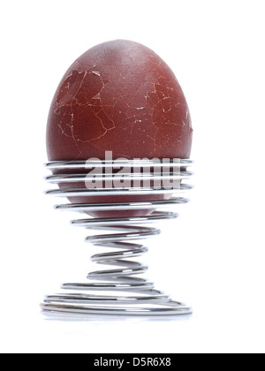 Dark brown soft-boiled egg with broken up egg shell in a spiral stand on white background Stock Photo