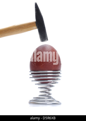 Egg with dark brown egg-shell on metal stand being hit by hammer shot on white background Stock Photo