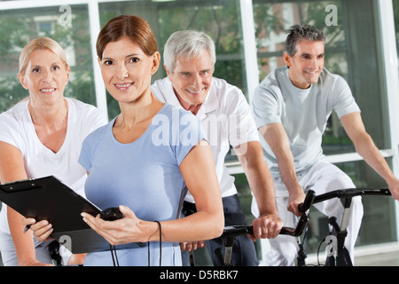 Fitness trainer coaching spinning exercise class with seniors in gym Stock Photo