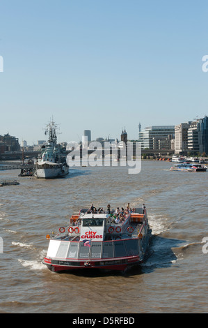 City cruise boat carrying tourists past HMS Belfast on the River Thames in the City of London, England. Stock Photo