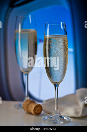 FIRST CLASS CABIN CHAMPAGNE FLYING CONCEPT Freshly poured French champagne in-flight in luxury aircraft cabin with window and aircraft wing behind Stock Photo