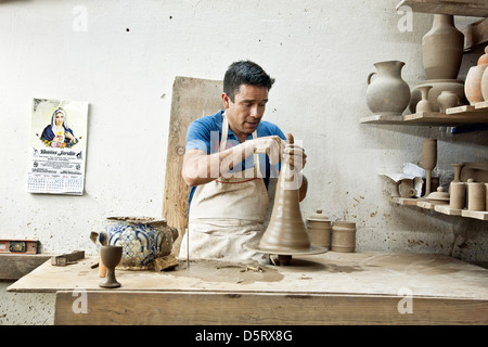 skilled potter craftsman turns Talavera clay on potters wheel as finished pieces cure on nearby shelves Uriarte factory Puebla Stock Photo