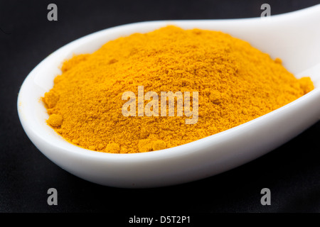 turmeric powder in white spoon on black table Stock Photo