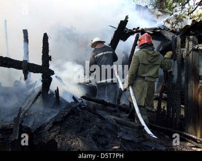 Smoldering remains of a ghetto house with a fireman spraying water firefighters extinguish a fire in an apartment house Stock Photo